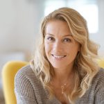 Porträt einer lächelnden blonden Frau im grauen Strickpullover auf gelbem Stuhl