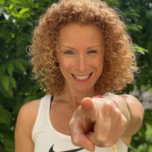 Lina, die fröhliche Babyschwimmleitung bei Babyschwimmen Hamburg, lächelt herzlich in die Kamera und zeigt direkt nach vorne – Motivation und Freude am Babyschwimmen